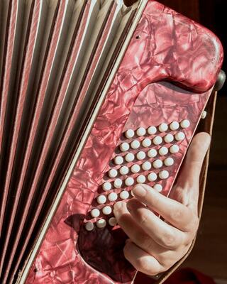 A close-up of a hand playing a vibrant red accordion, showcasing its intricate buttons and textured body.