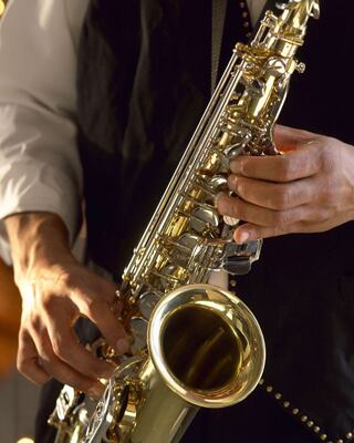 A musician plays a shiny saxophone, showcasing intricate keys and a vibrant shine, dressed in a black vest and white shirt.