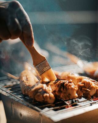 man placing barbeque on chicken while grilling
