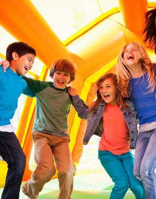 Four children joyfully jump together in a colorful inflatable play structure, filled with laughter and vibrant energy.
