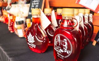 Bottles of maple syrup with various labels and designs are neatly arranged on a table, showcasing their rich amber color.