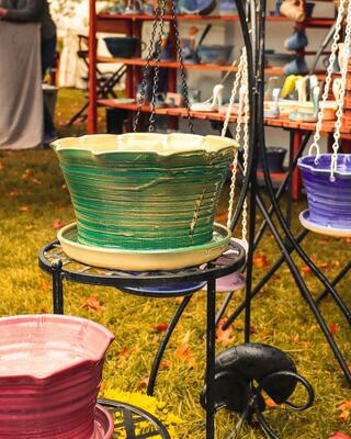 Colorful hanging and standing pots showcase vibrant designs in a quaint outdoor market setting, with green, pink, and purple hues.