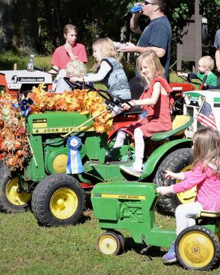 Children enjoy riding decorated toy tractors while adults watch nearby, creating a lively and festive atmosphere.