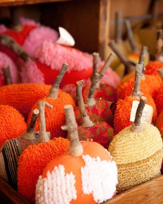 A collection of decorative pumpkins in vibrant colors, topped with twig stems, is arranged neatly on a wooden shelf.