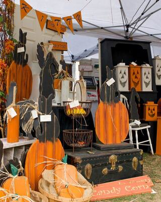 A festive display of wooden pumpkins and Halloween decorations, featuring orange and black colors, set under a tent with autumn decor.