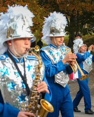 Marching band members in vibrant blue uniforms with silver accents and feathered hats perform together, showcasing their musical talents.