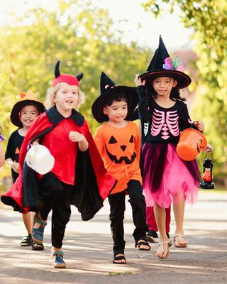 A group of children dressed in vibrant Halloween costumes, joyfully walking together in a festive outdoor setting.