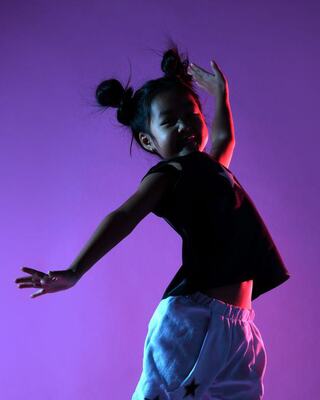 A joyful child dances with enthusiasm, sporting a playful outfit against a vibrant purple background.