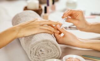 A person receives a manicure, hands resting on a towel, surrounded by nail polish and beauty products, creating a soothing salon atmosphere.