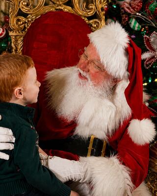 A joyful child sits on Santa's lap, sharing a moment of wonder in a festive, holiday setting, adorned with Christmas decorations.