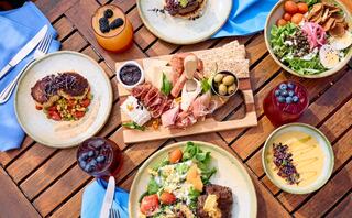 A picturesque spread of gourmet dishes, including salads, meats, and desserts, set on a wooden table with vibrant drinks.