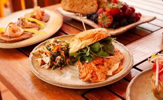 A delicious plate features a grilled salmon sandwich with greens, accompanied by a fresh slaw and a side of colorful fruits.