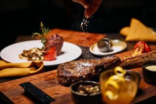 A perfectly cooked steak being seasoned, with gourmet side dishes and garnishes elegantly arranged for a fine dining experience.