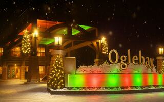 A charming entrance to Oglebay, featuring a welcoming sign and a vintage trolley, set against a colorful sunset sky and lush greenery.