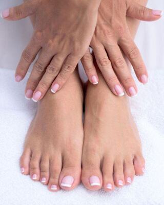 A pair of manicured hands rests on elegantly pedicured feet, both featuring a soft pink polish, set against a white background.