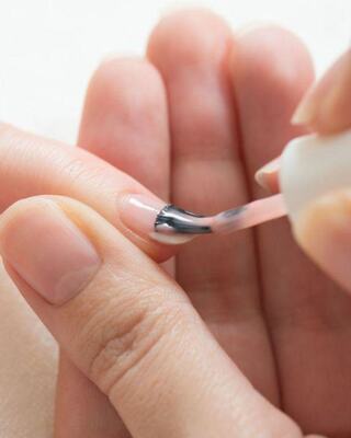 A person applies a glossy, light nail polish to a fingernail, showcasing a meticulous manicure process.