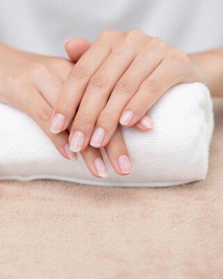 Delicately manicured hands rest atop a soft white towel, showcasing a natural, polished look against a beige background.