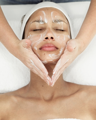 A woman receives a facial treatment, with hands gently massaging cleanser into her skin, promoting relaxation and skincare.
