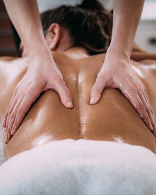 A person receives a relaxing massage, with hands applying gentle pressure on their back, glistening with oil, in a serene setting.