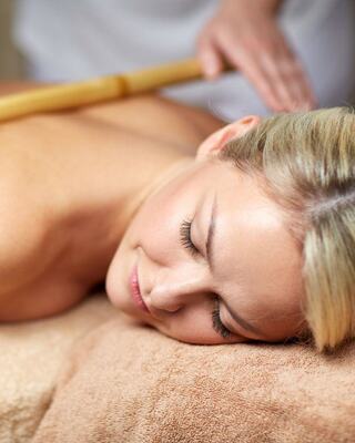 A relaxed woman receives a bamboo massage, eyes closed, enjoying a soothing experience in a tranquil spa setting.
