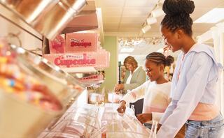 Two girls enjoy selecting treats from a colorful candy display while an adult observes in a cheerful shop filled with sweets.
