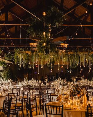 A beautifully decorated venue with elegant tables, lush greenery, and warm ambient lighting creates a romantic and inviting atmosphere.