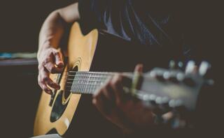 A person strums an acoustic guitar, focusing on the chords with fingers positioned on the strings, creating a musical atmosphere.