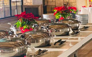 A buffet setup features shiny serving dishes with lids, elegant utensils, and festive poinsettias adding a touch of color.