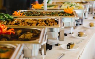 An array of buffet dishes featuring meats, vegetables, and garnishes, elegantly displayed with vibrant orange flowers for decoration.