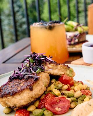 Delicious crab cakes topped with microgreens, served with vibrant veggies and a refreshing cocktail in a lively dining setting.