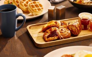 A cozy breakfast spread featuring pastries, a cup of coffee, and waffles, set on a wooden table with savory options visible in the background.