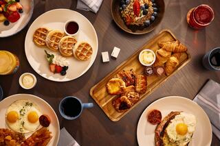 A cozy breakfast spread featuring pastries, a cup of coffee, and waffles, set on a wooden table with savory options visible in the background.