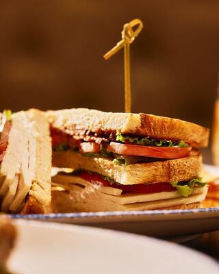 A stacked sandwich featuring layers of turkey, lettuce, tomato, and a crispy element, secured with a toothpick, served with rustic bread.