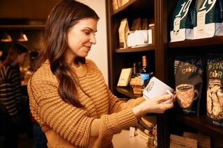 A woman in a cozy sweater inspects a product while shopping in a store filled with various packaged items.